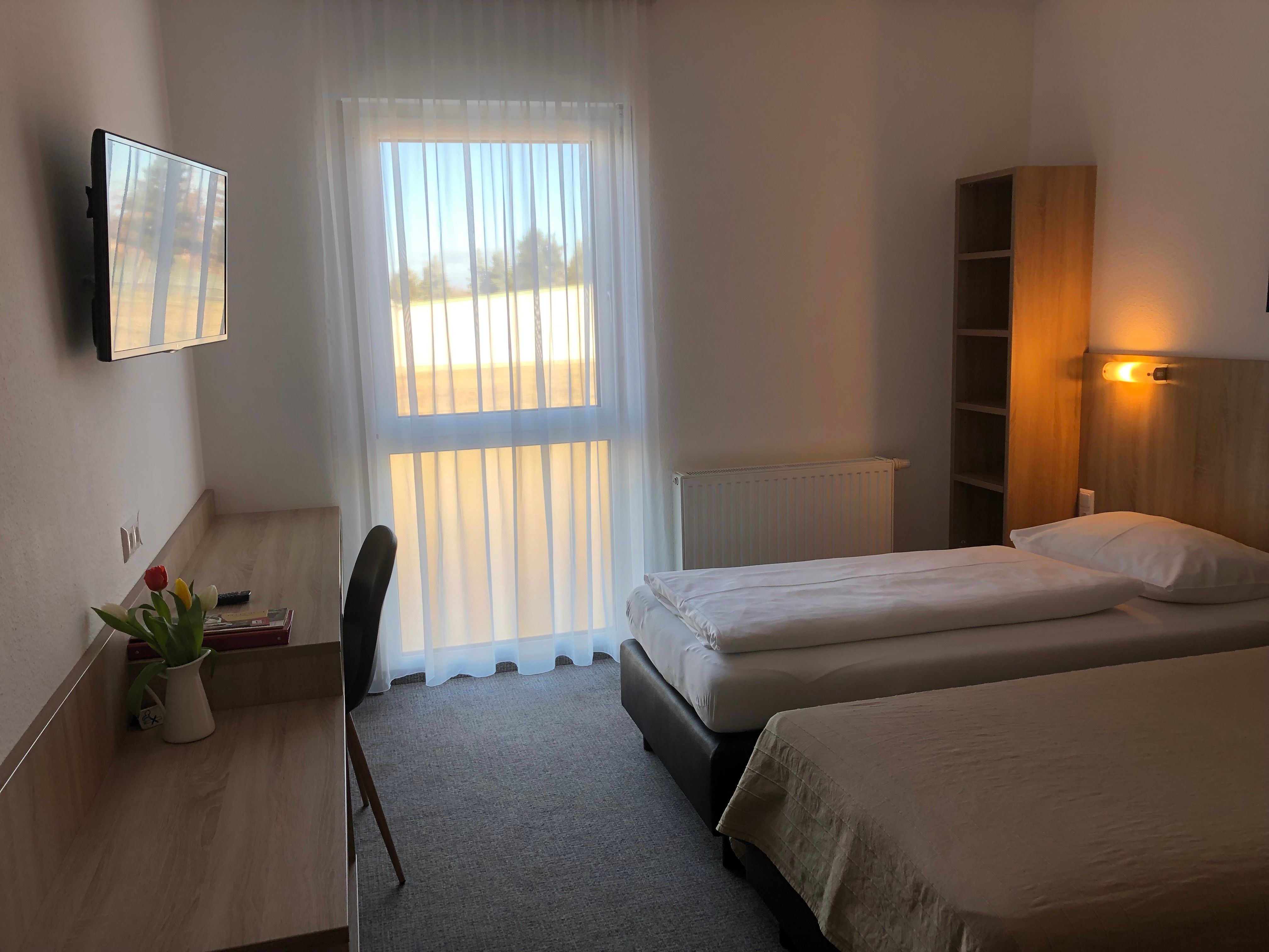 Ein schlicht eingerichtetes Motelzimmer mit zwei Einzelbetten, einem Schreibtisch, einem Fernseher und einem Fenster mit Vorhängen.