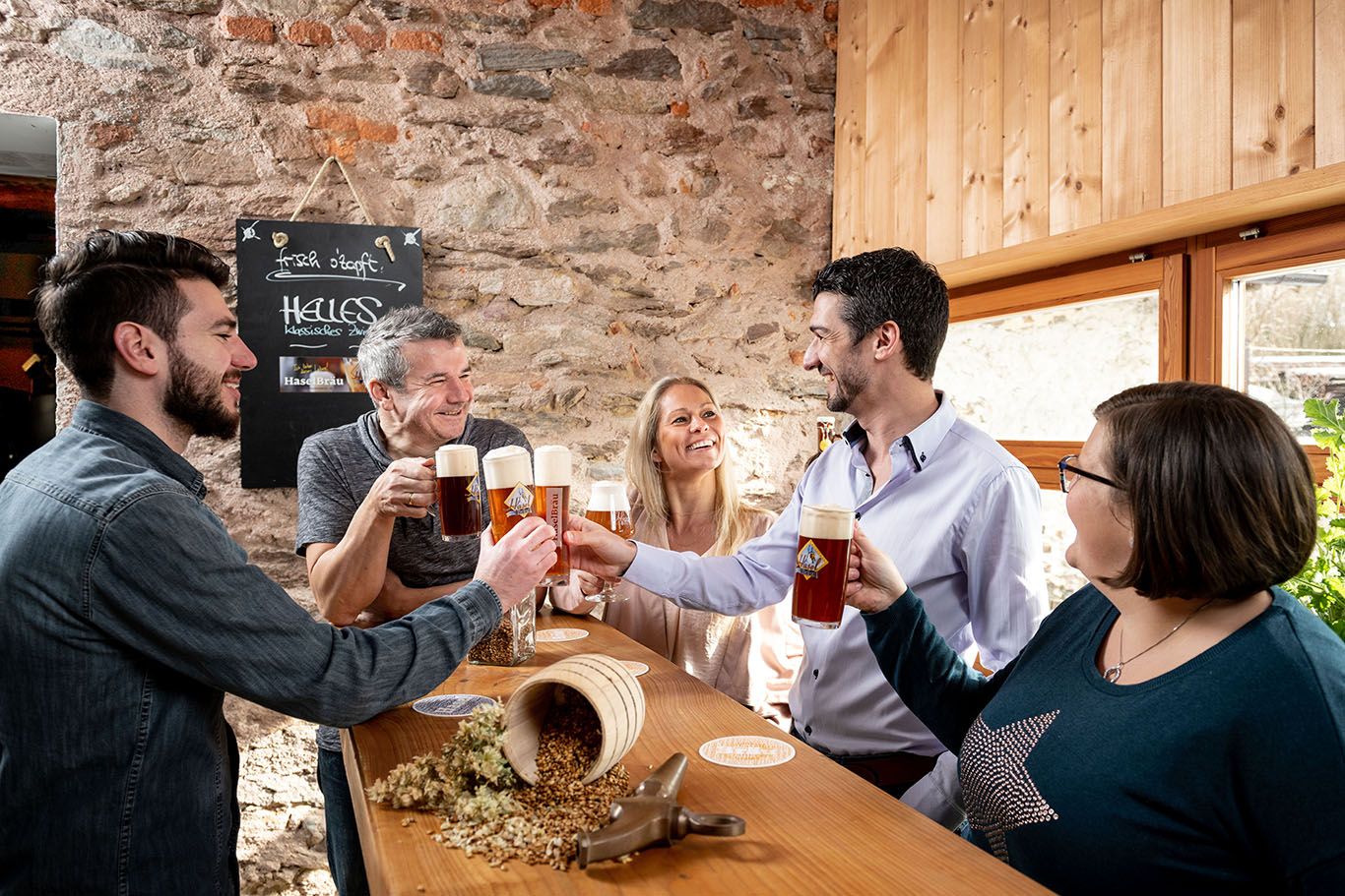 Gruppe von Menschen stößt mit Bierkrügen in einer rustikalen Brauerei an.
