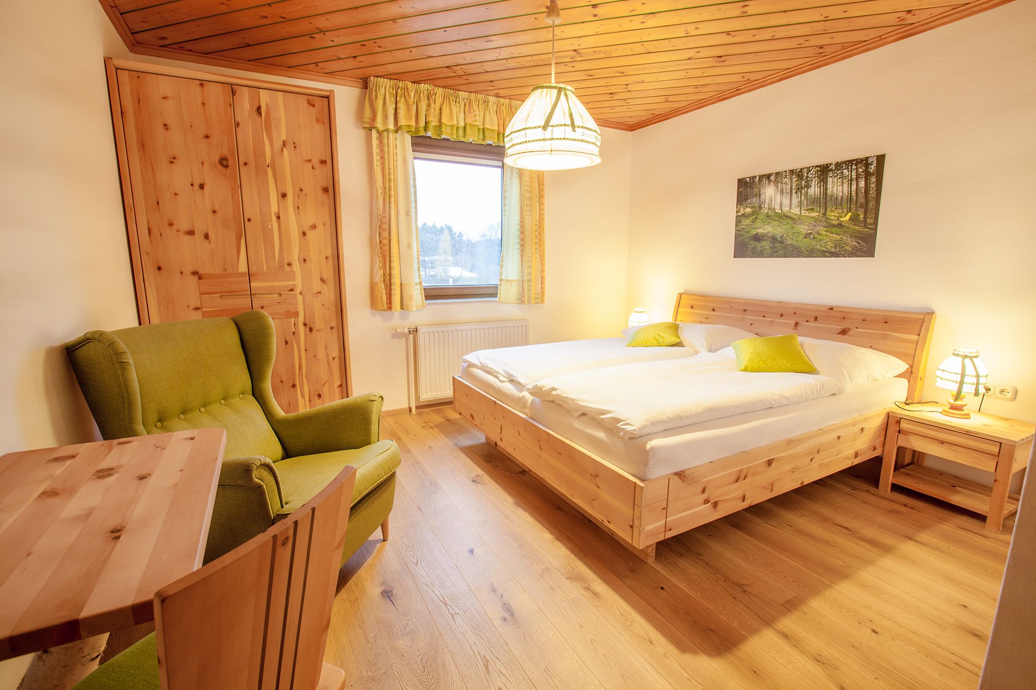 Gemütliches Schlafzimmer mit Holzmöbeln, einem Doppelbett, grünem Sessel und einem Fenster mit Vorhängen.