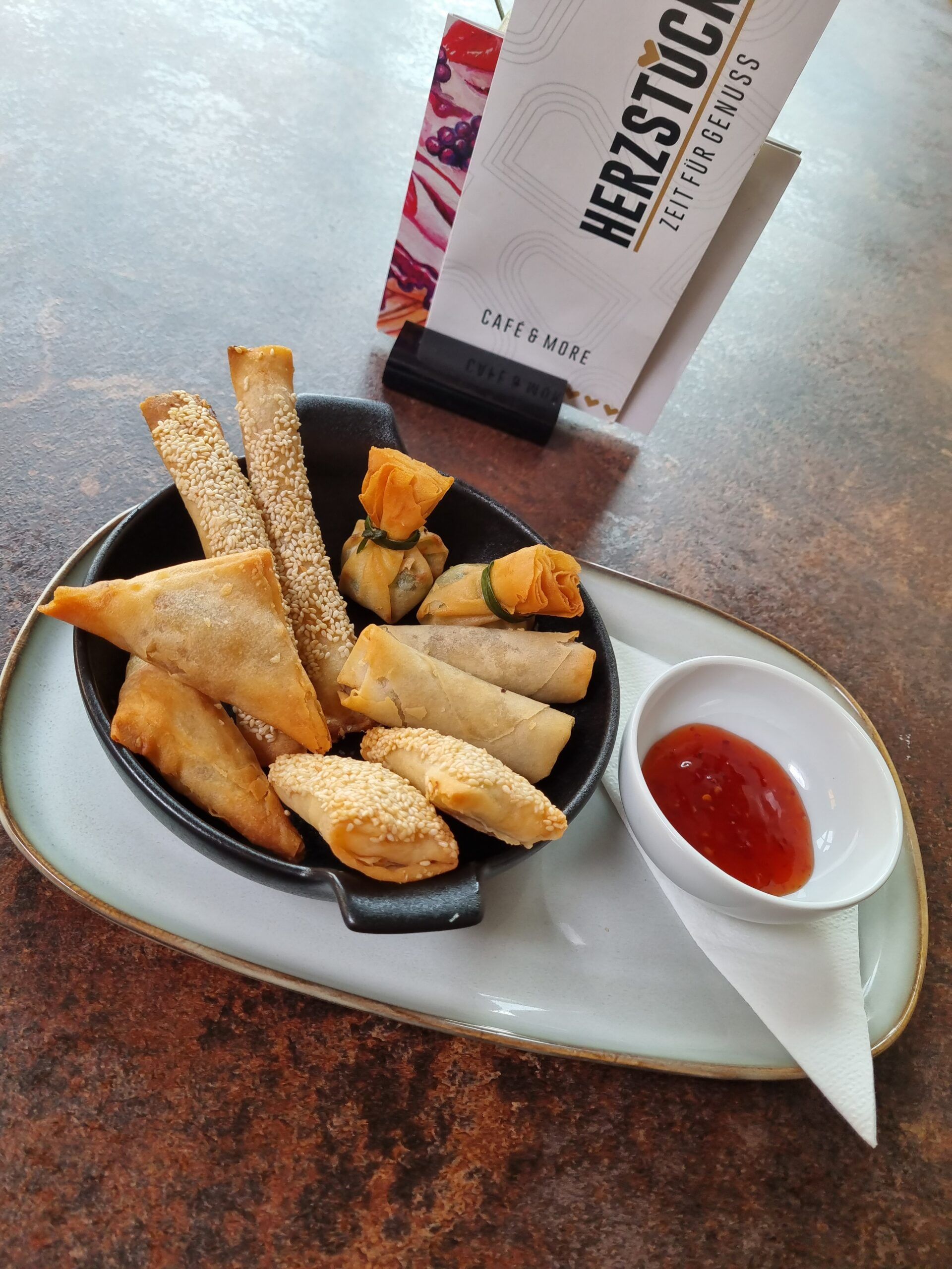 Verschiedene frittierte Snacks auf einem Teller mit Dip und Café Herzstück Menü im Hintergrund.