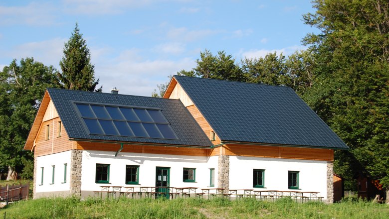 Eibl-Teichhütte, © Fam. Tröstl Eine Hütte mit Solarpanelen auf dem Dach, umgeben von Bäumen und Wiese.