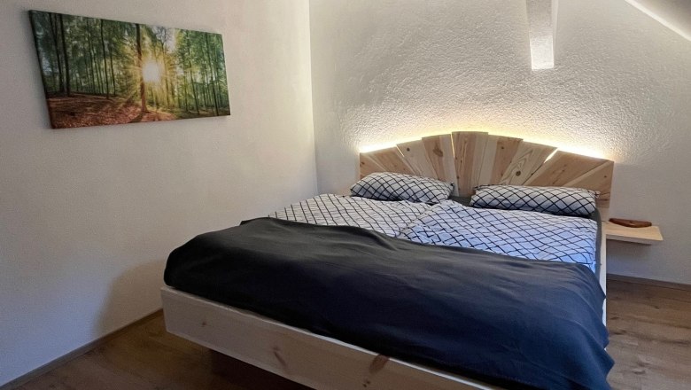Ein gem&uuml;tliches Schlafzimmer mit einem Holzbett, einem Bild von einem Wald an der Wand und einem wei&szlig;en Teppich auf dem Holzboden.