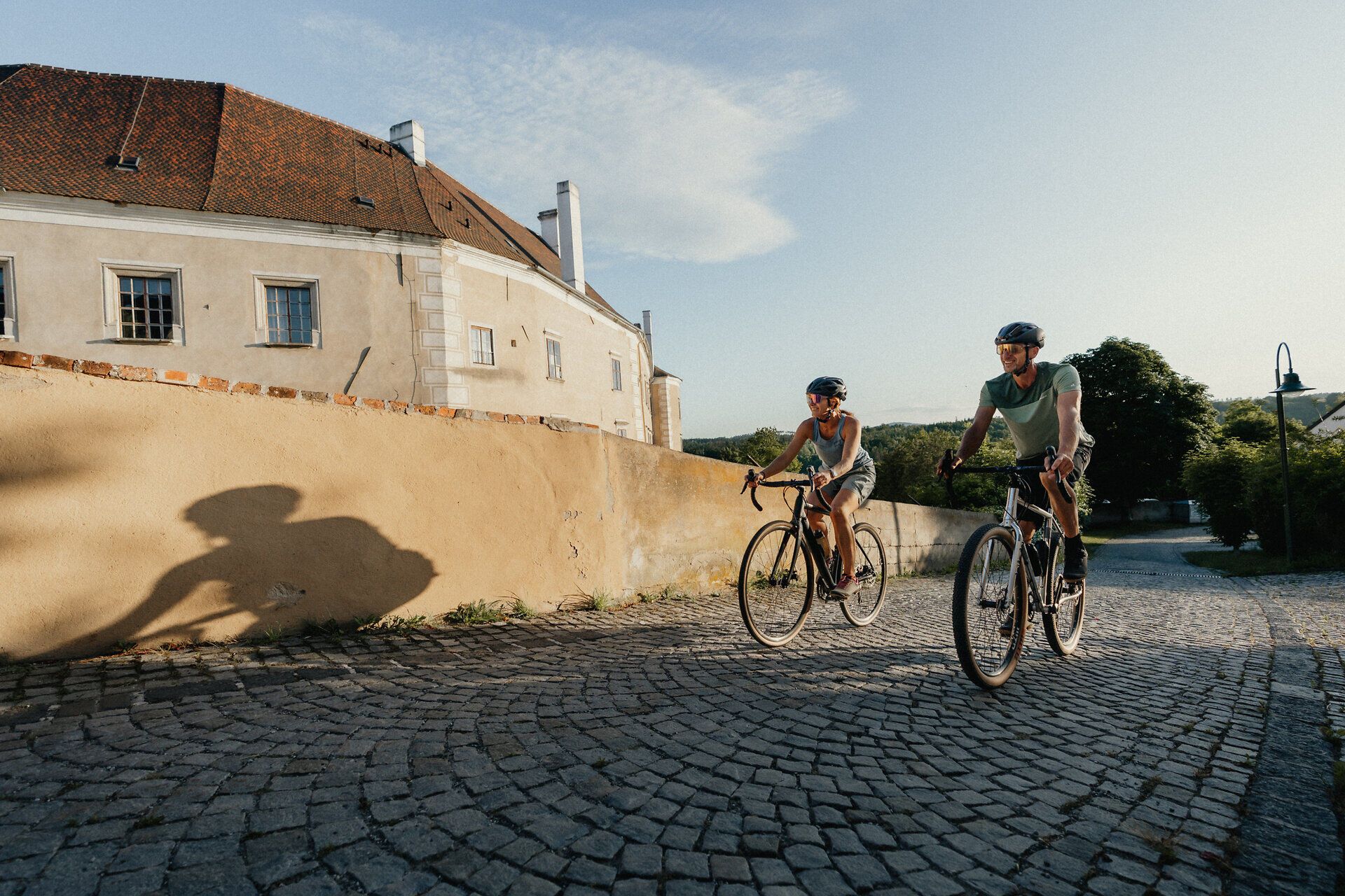 Zwei Radfahrer fahren auf einer gepflasterten Straße entlang einer alten Stadtmauer in Drosendorf.
