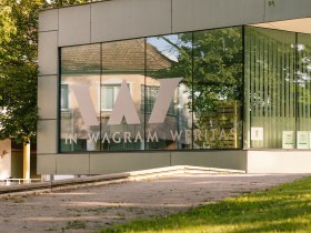 Die moderne Vinothek strahlt eine einladende Atmosph&auml;re aus, umgeben von &uuml;ppigem Gr&uuml;n und sanften H&uuml;geln. Hier k&ouml;nnen Besucher die erlesenen Weine der Region genie&szlig;en und sich von der Sch&ouml;nheit der Landschaft verzaubern lassen.