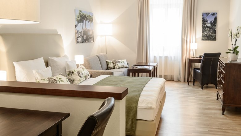 Helles, gemütliches Hotelzimmer mit Bett, Sofa, Schreibtisch und Dekoration.