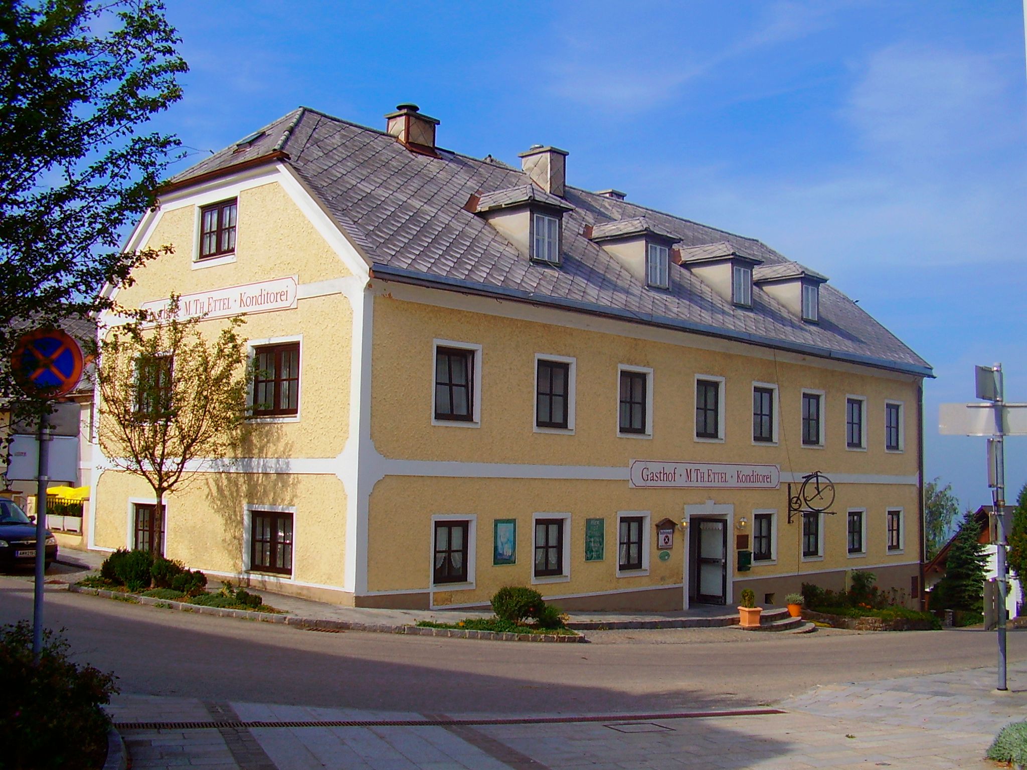 Gelbes zweistöckiges Gebäude mit der Aufschrift 'Gasthof M. Th. Ettel Konditorei'.