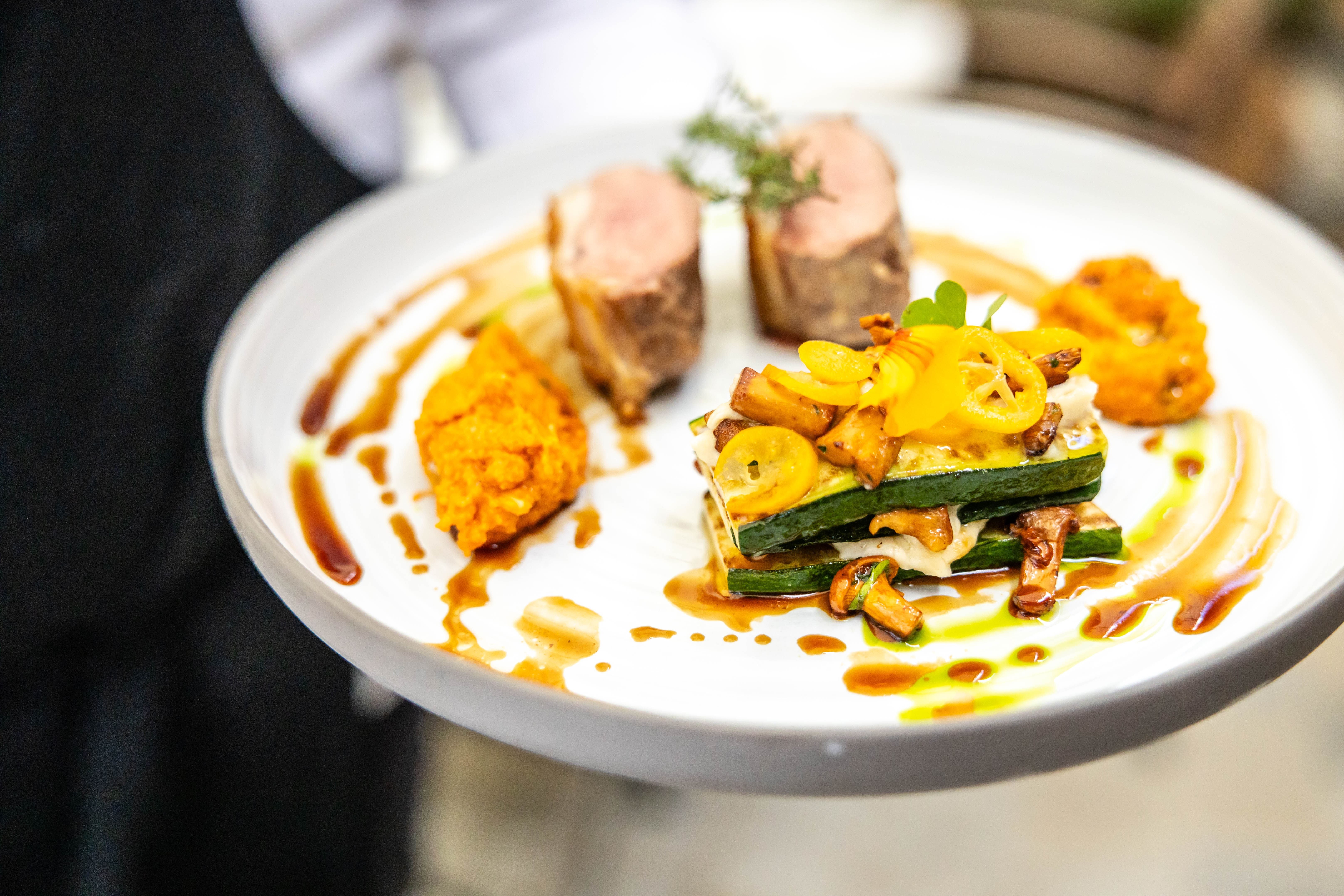 Ein Gourmetgericht auf einem weißen Teller, bestehend aus Fleisch, Gemüse und Soße, kunstvoll angerichtet.