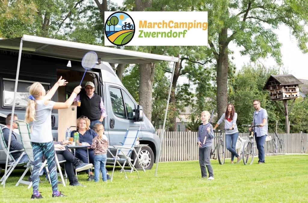 Familie beim Camping mit Wohnmobil und Badmintonspiel auf einer Wiese.