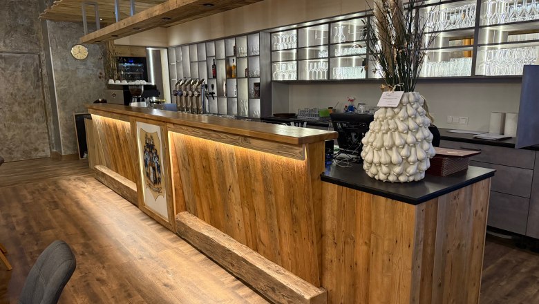 Restaurant Osterbauer, © Thomas Osterbauer Holztheke in einem Restaurant mit dekorativer Vase und Gläserregal im Hintergrund.