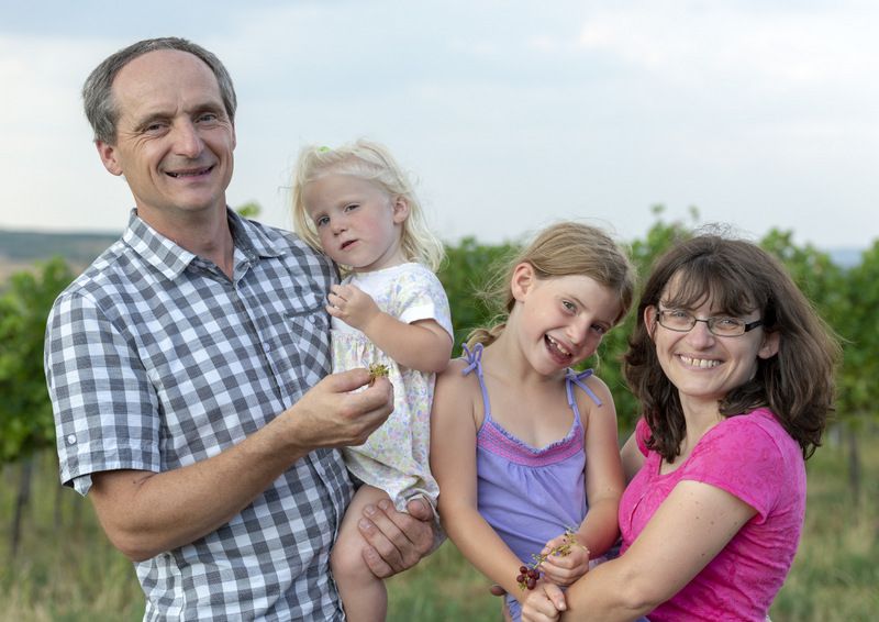 Eine Familie steht lächelnd in einem Weinberg.