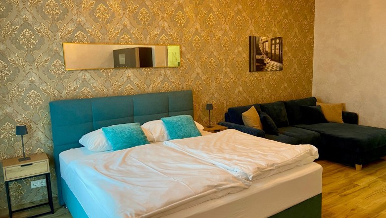 Elegantes Hotelzimmer mit Doppelbett, blauer Couch und goldener Tapete.