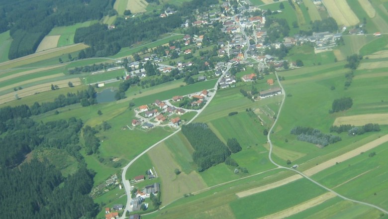 Luftaufnahme einer l&auml;ndlichen Ortschaft mit Feldern und W&auml;ldern.