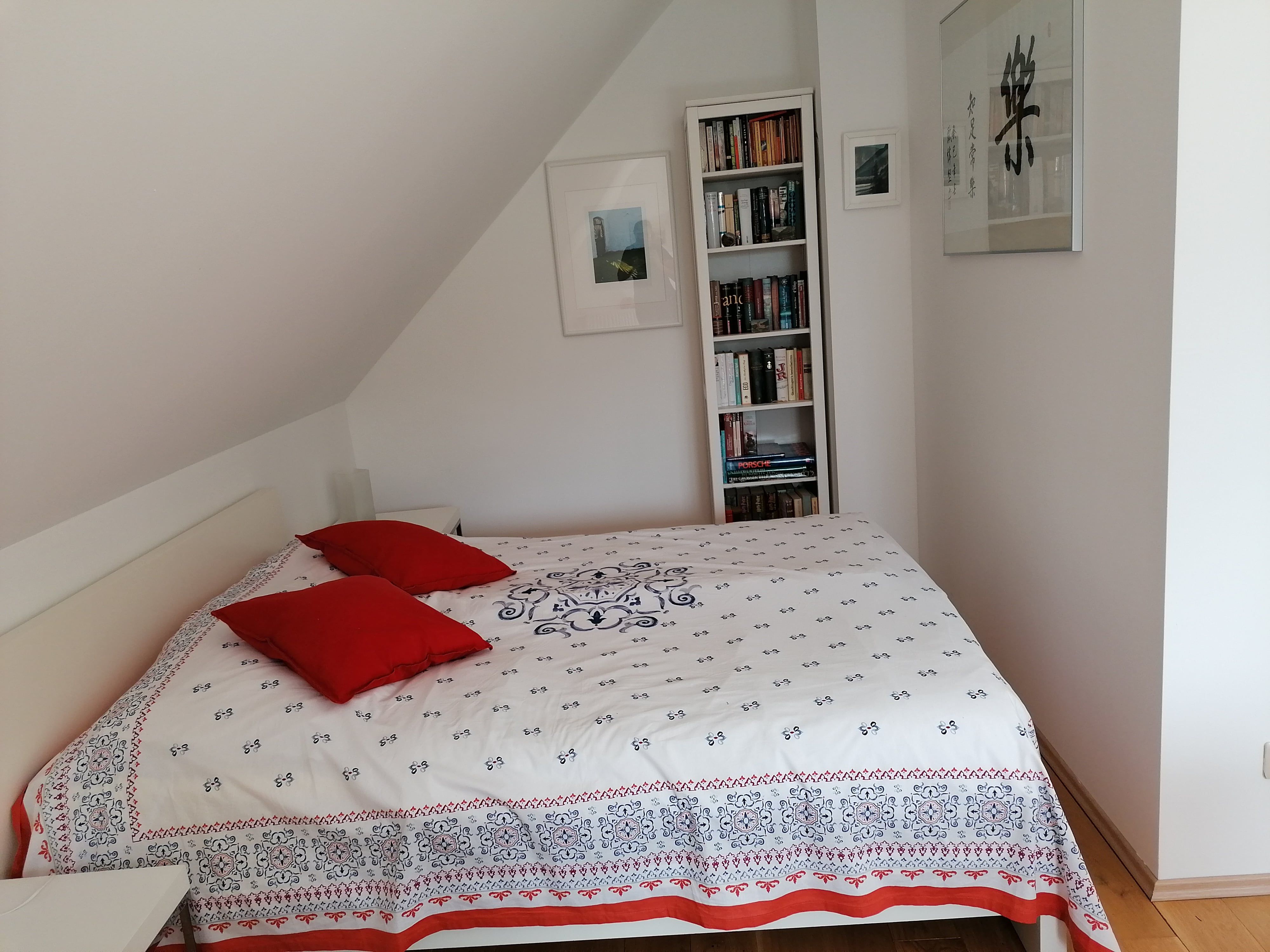 Schlafzimmer mit Bett, roten Kissen und Bücherregal.