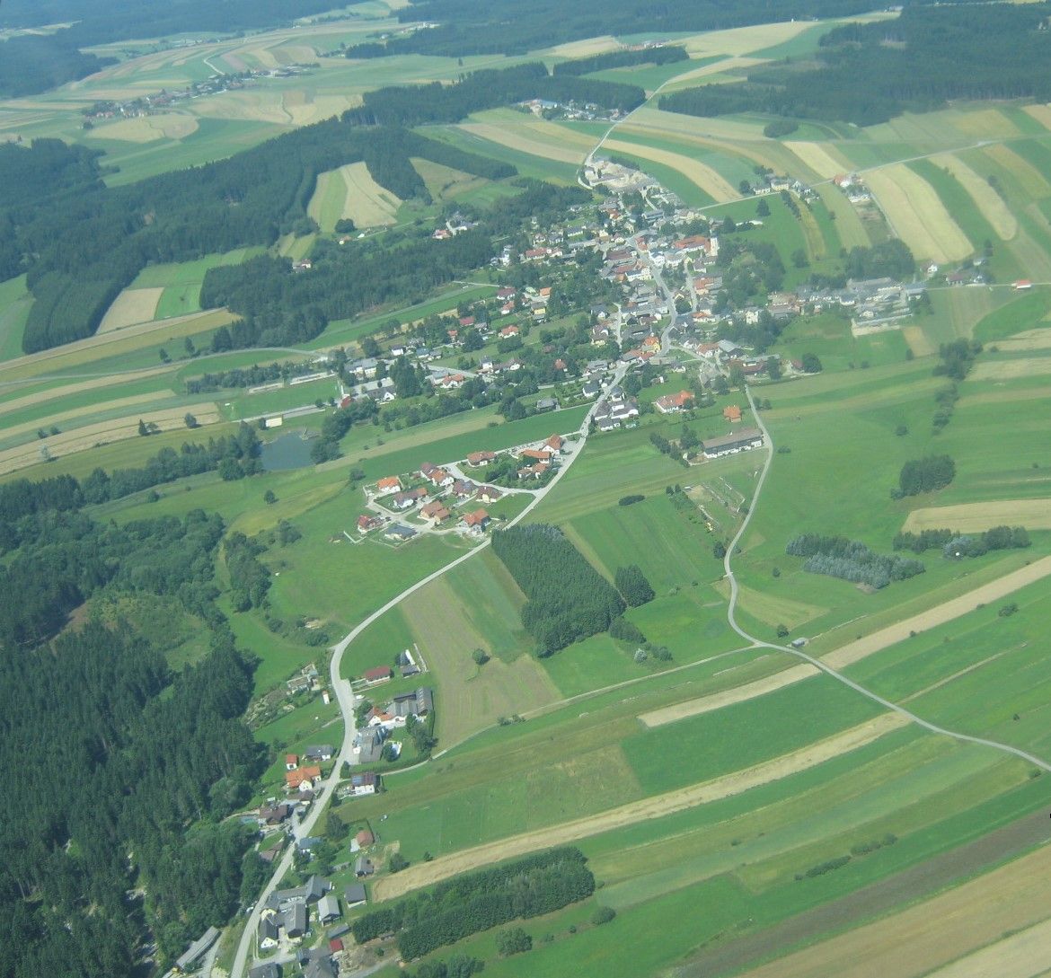 Luftaufnahme einer ländlichen Ortschaft mit Feldern und Wäldern.