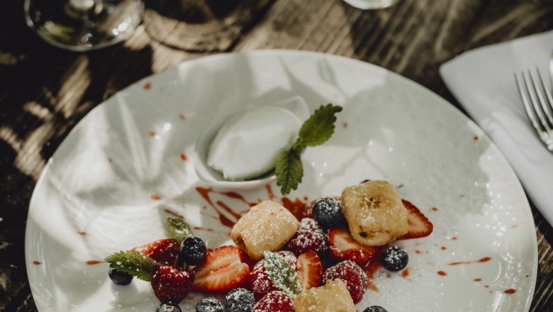 Ein Dessertteller mit gebackenem Topfen, marinierten Beeren und Joghurteis, dekoriert mit Minzblättern, auf einem Holztisch.