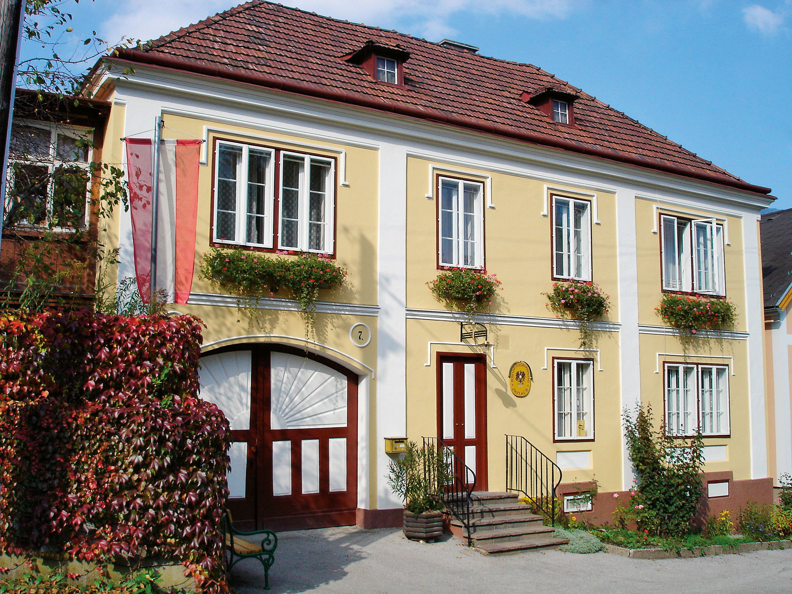Historisches gelbes Gebäude mit roten Fensterläden und Blumen, beschriftet als Kaiserpostamt.