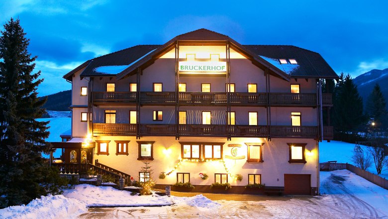 Pension Bruckerhof, © Franz Zwickl Beleuchtetes Gebäude der Pension Bruckerhof im Schnee bei Dämmerung.