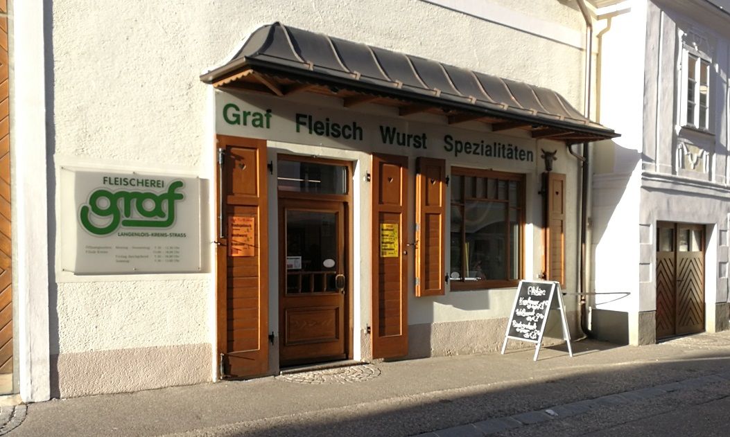 Außenansicht der Fleischerei Graf mit Holztüren und Werbetafel.