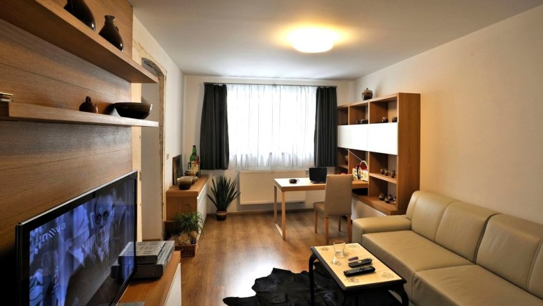 Modern eingerichtetes Wohnzimmer mit Sofa, Fernseher, Schreibtisch und Regalen.