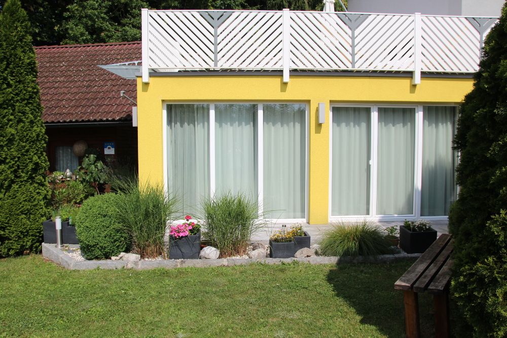 Gelbes Gartenappartement mit großen Fenstern und gepflegtem Garten.