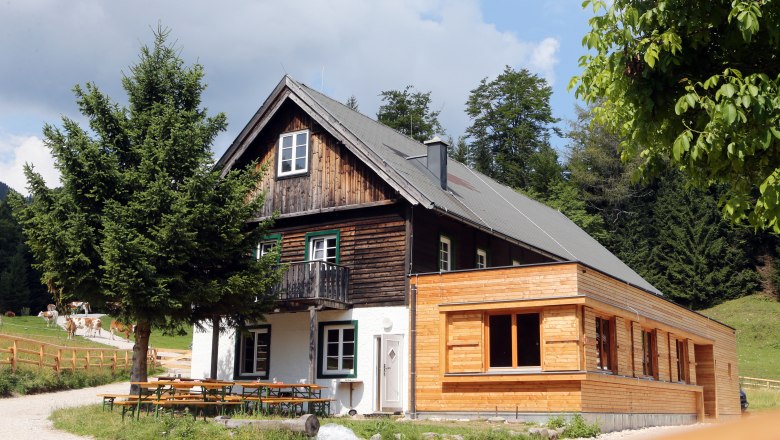 Schutzhaus Vorderötscher, © weinfranz.at Ein traditionelles Holzhaus mit Anbau in einer ländlichen Umgebung, umgeben von Bäumen und Wiesen.