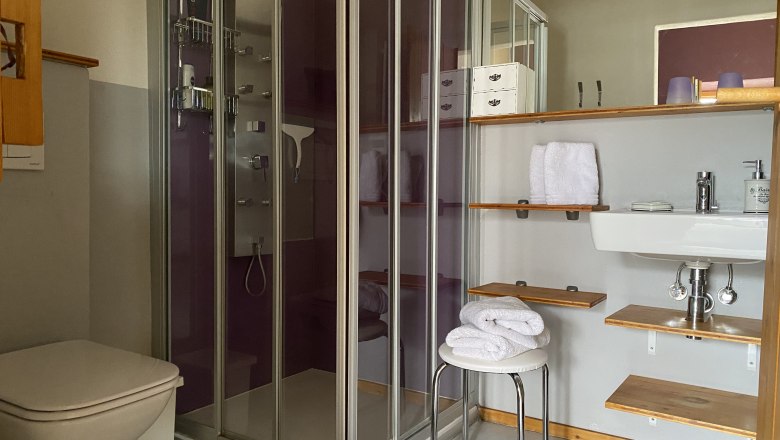 Modernes Badezimmer mit Dusche, Waschbecken, Handtüchern und Regalen.