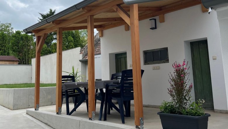 &Uuml;berdachte Terrasse mit Tisch und St&uuml;hlen, umgeben von Pflanzen.