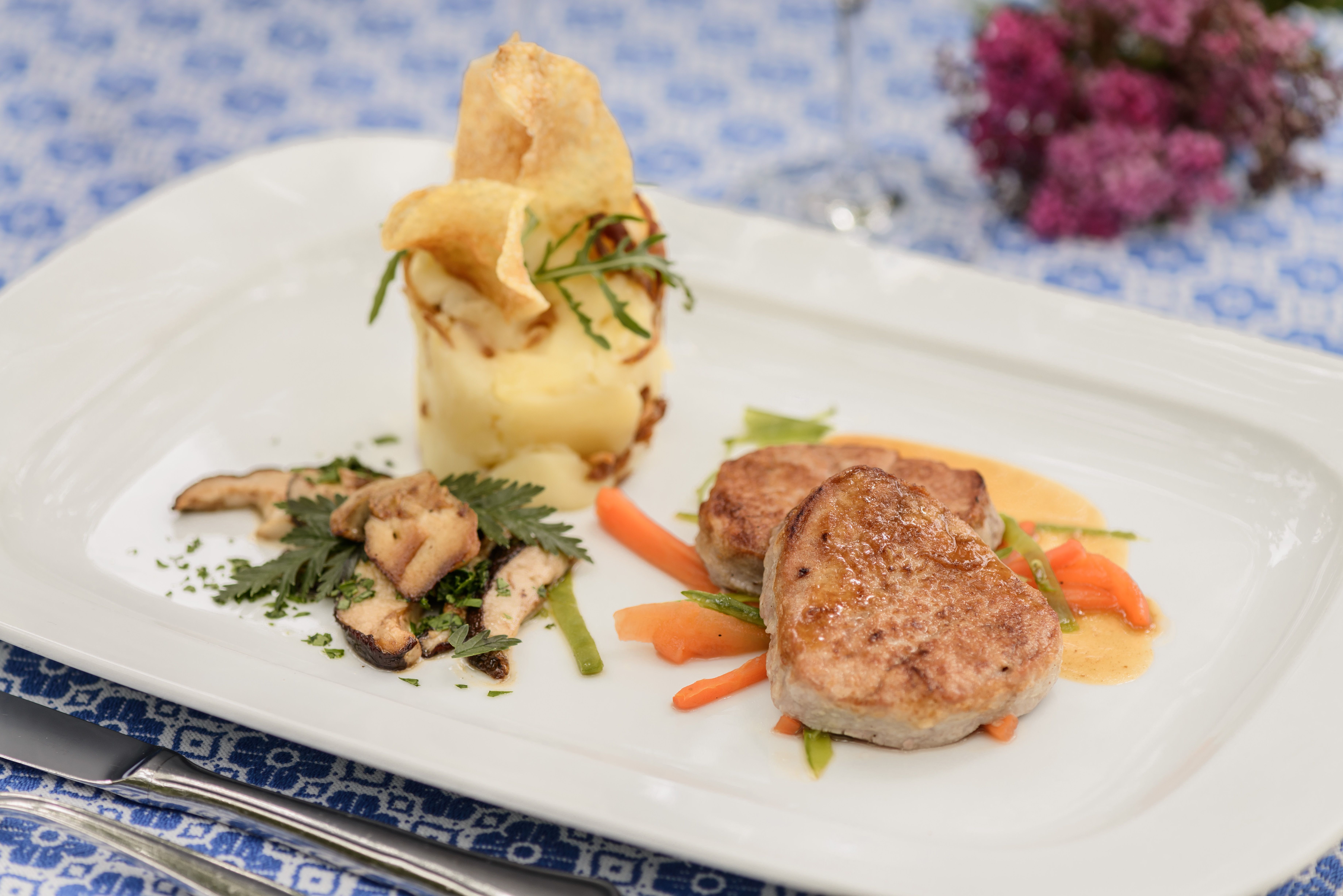 Gourmetgericht mit Fleisch, Kartoffelpüree und Gemüse auf weißem Teller.