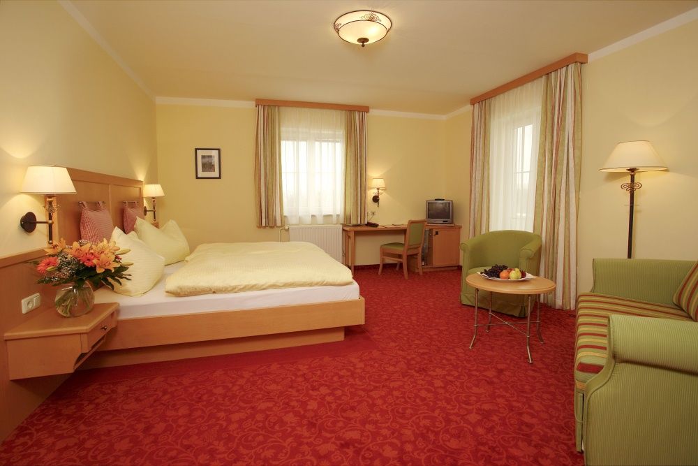 Ein gemütliches Hotelzimmer mit Doppelbett, Sofa, Tisch und Fernseher. Gelbe Wände und rote Teppiche dominieren das Zimmer.