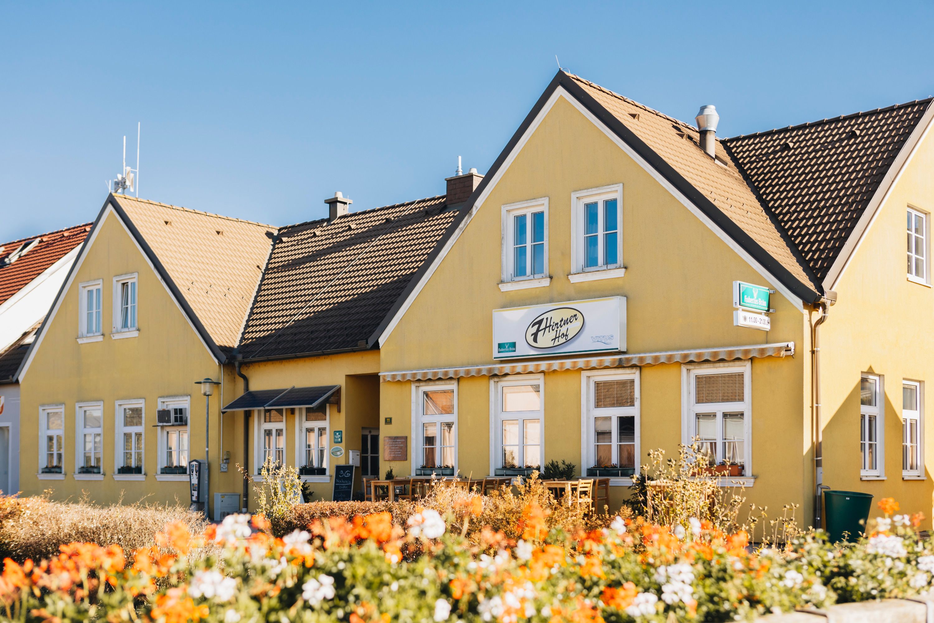 Gelbes Wirtshaus mit Blumen im Vordergrund.