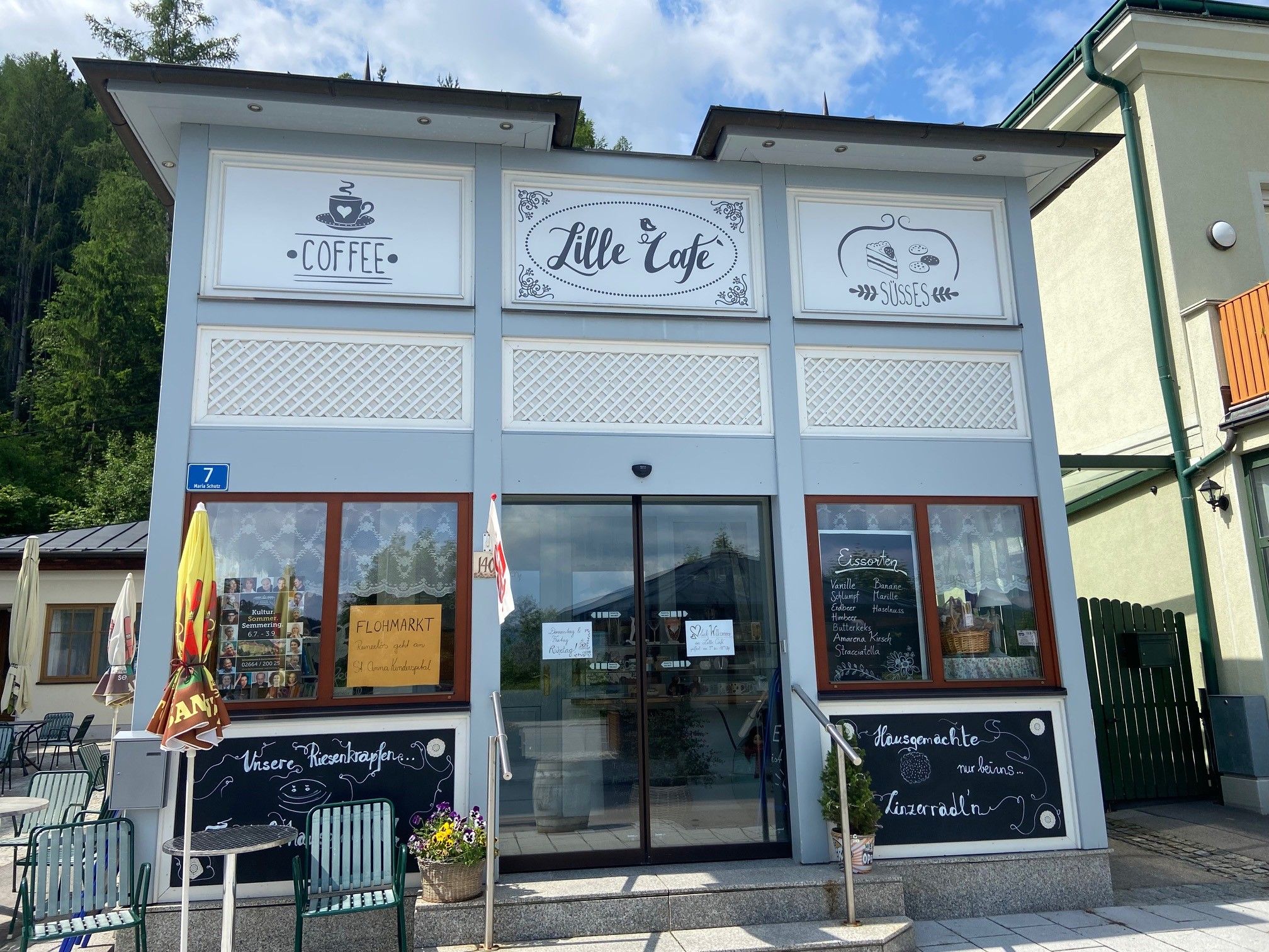 Außenansicht eines Cafés mit Schildern für Kaffee und Süßes.