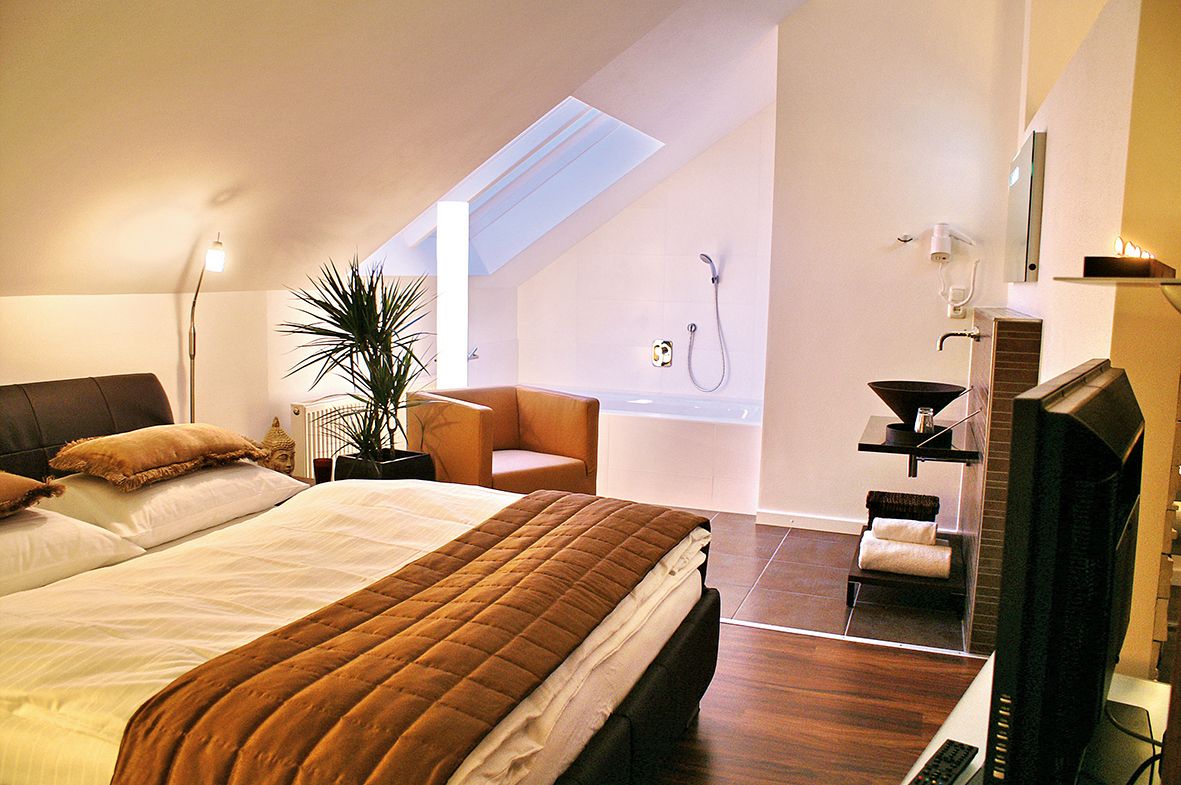 Gemütliches Schlafzimmer mit Doppelbett, Pflanzen, Sessel und Badewanne unter Dachschräge.