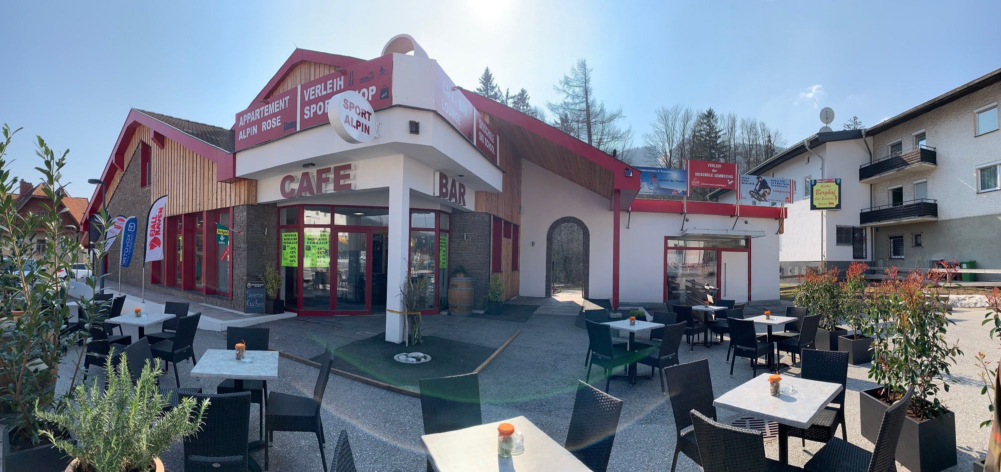 Außenansicht einer Café-Bar mit Terrasse und Sitzgelegenheiten im Freien.