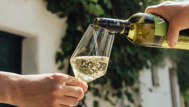 Eine Hand gie&szlig;t Wei&szlig;wein aus einer Flasche in ein Glas, das von einer anderen Hand gehalten wird.