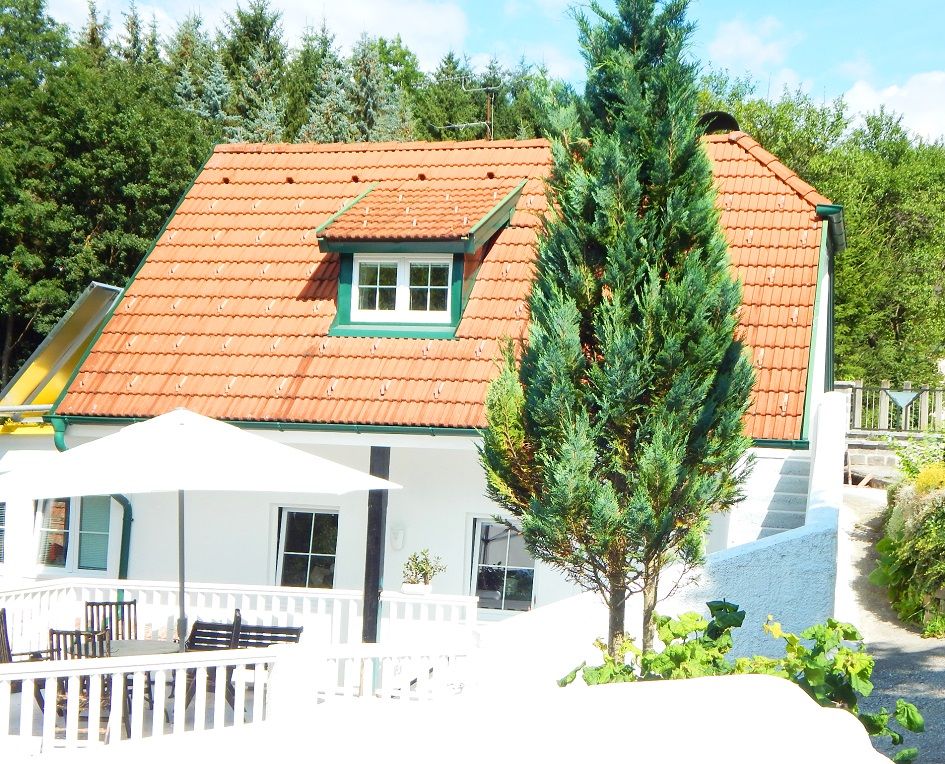 Außenansicht eines weißen Ferienhauses mit rotem Dach und Terrasse.