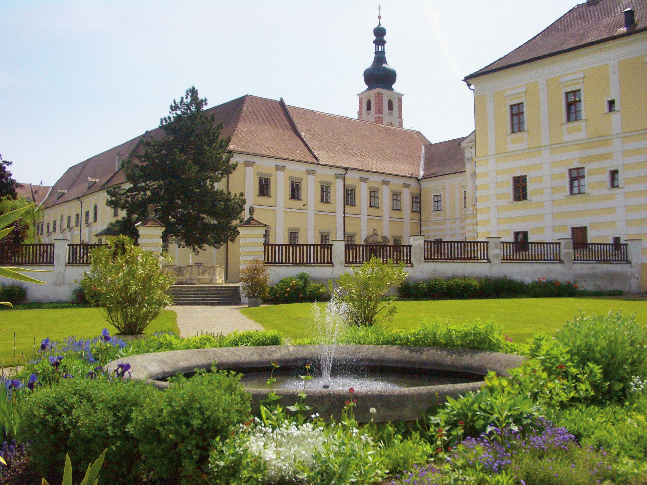 Historisches Klostergebäude mit Garten und Springbrunnen.