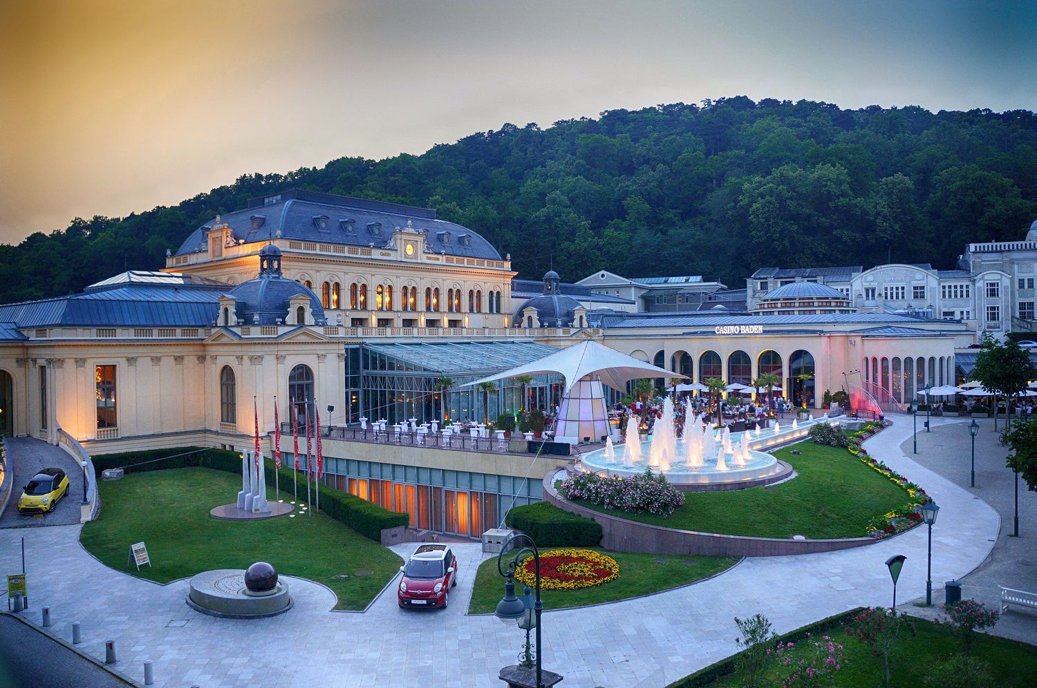 Außenansicht des Congress Centers Baden mit beleuchtetem Springbrunnen und umliegender Natur.