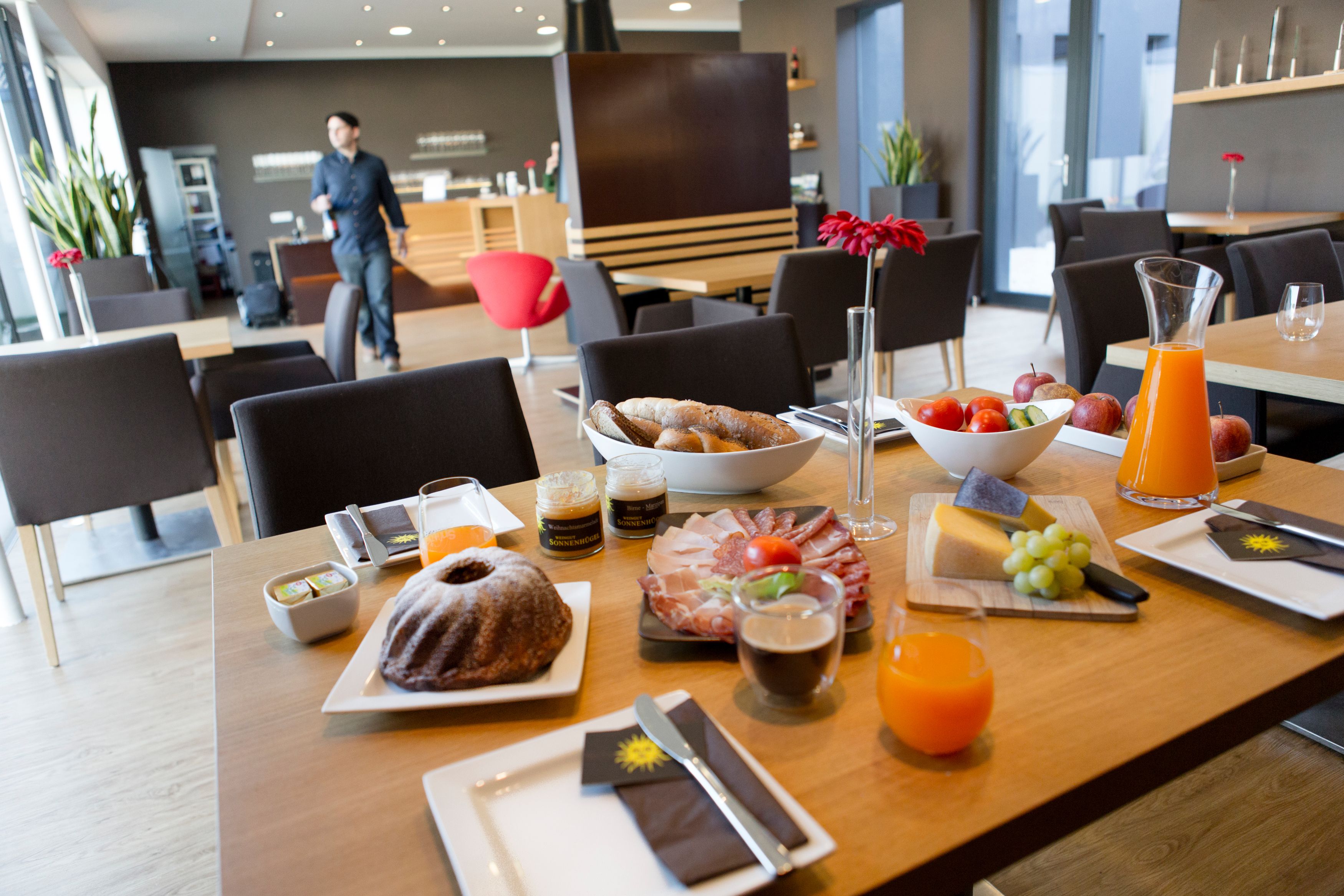 Frühstückstisch mit Gebäck, Aufschnitt, Käse, Obst und Saft in einem modernen Café.