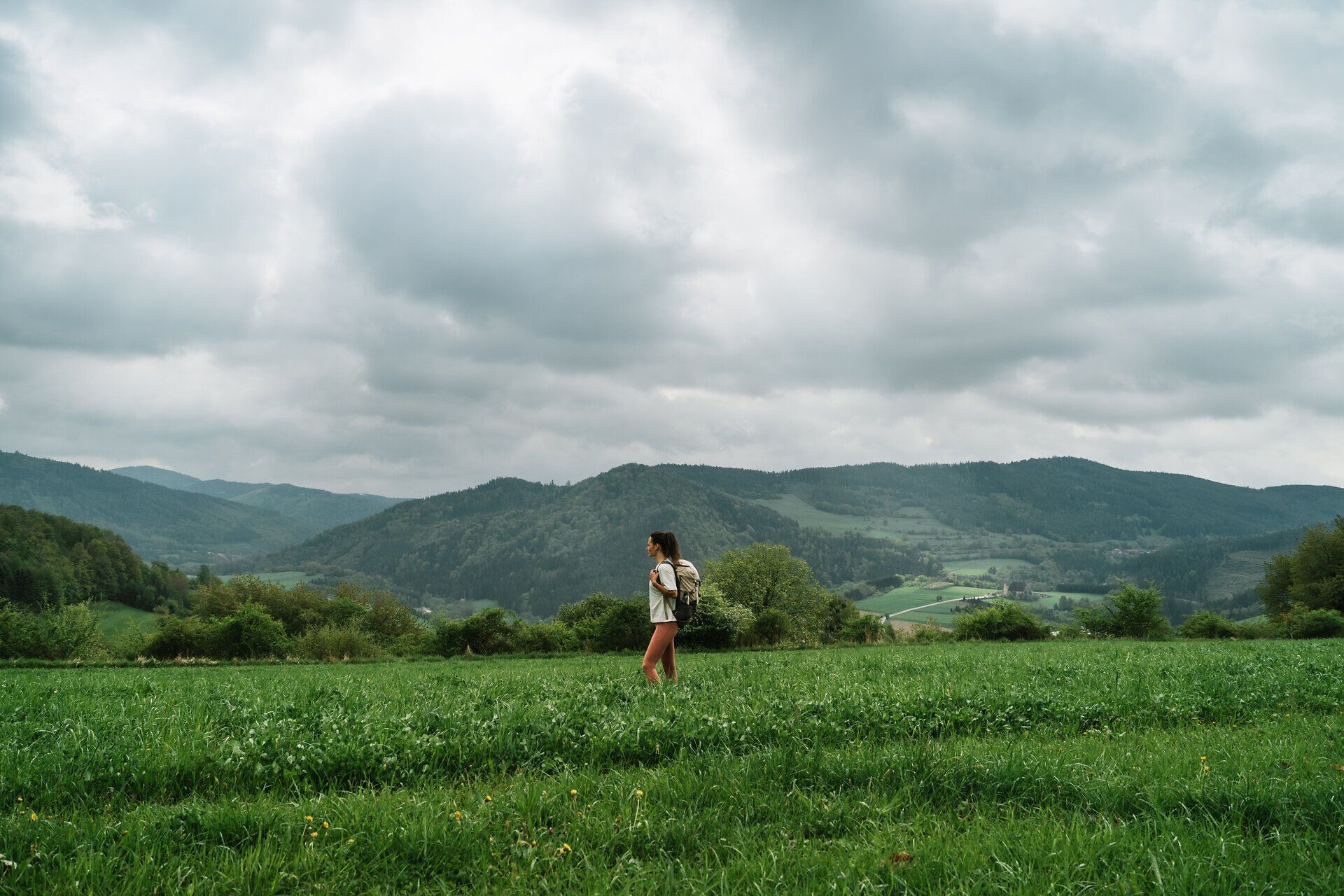 Ein sanfter Wind streicht über die weiten Wiesen, während die Wolken über die majestätischen Berge ziehen. Die Wanderin genießt die frische Luft und die atemberaubende Aussicht, die die Natur hier bietet. Ein perfekter Ort, um die Seele baumeln zu lassen und die Schönheit der Landschaft zu erleben.