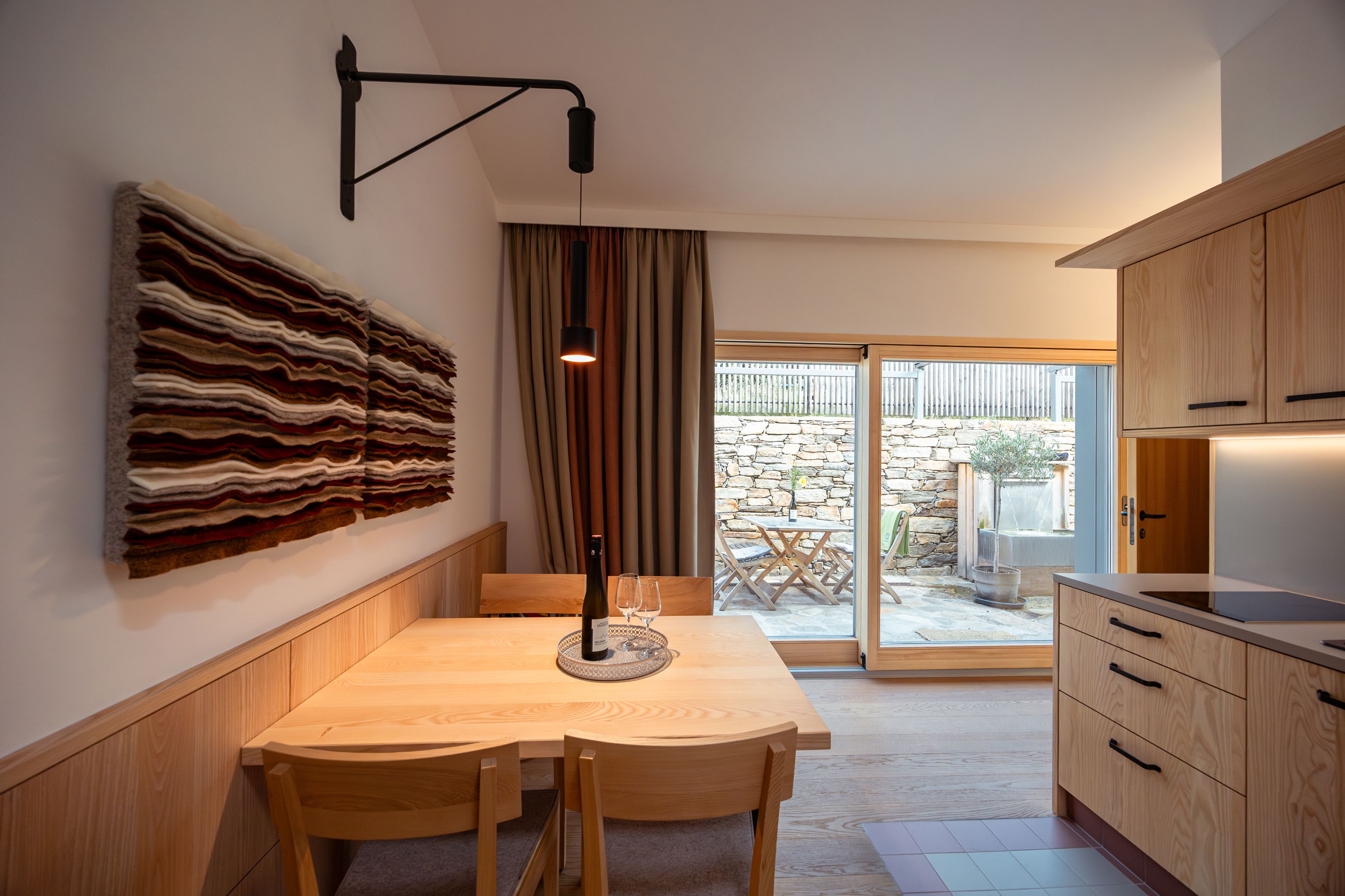 Innenansicht eines modernen Essbereichs mit Holzmöbeln und Wandkunst, Blick auf eine Terrasse durch eine Glastür.