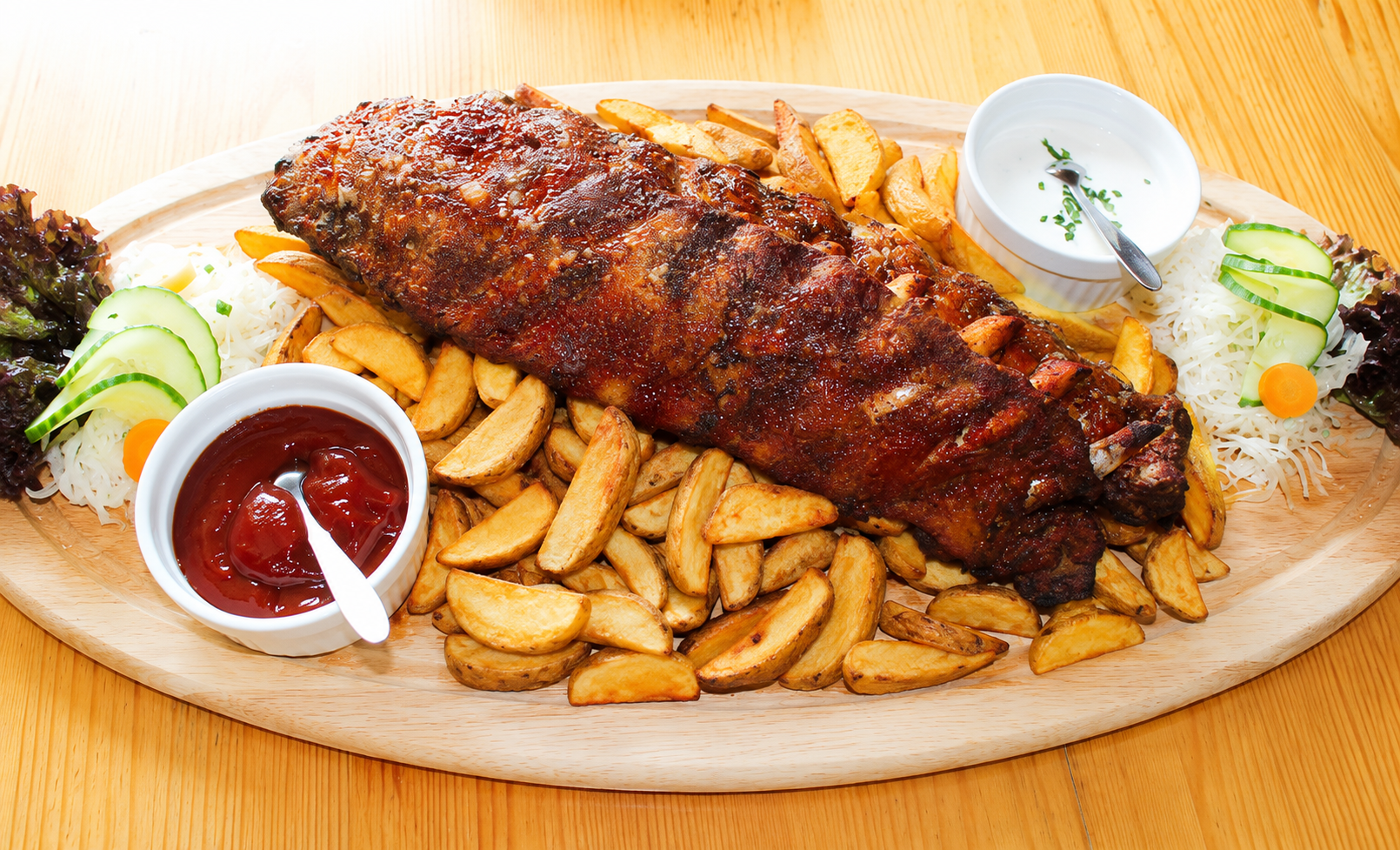 Ein Teller mit knusprigen Spareribs, Kartoffelspalten, Salat und Dips.