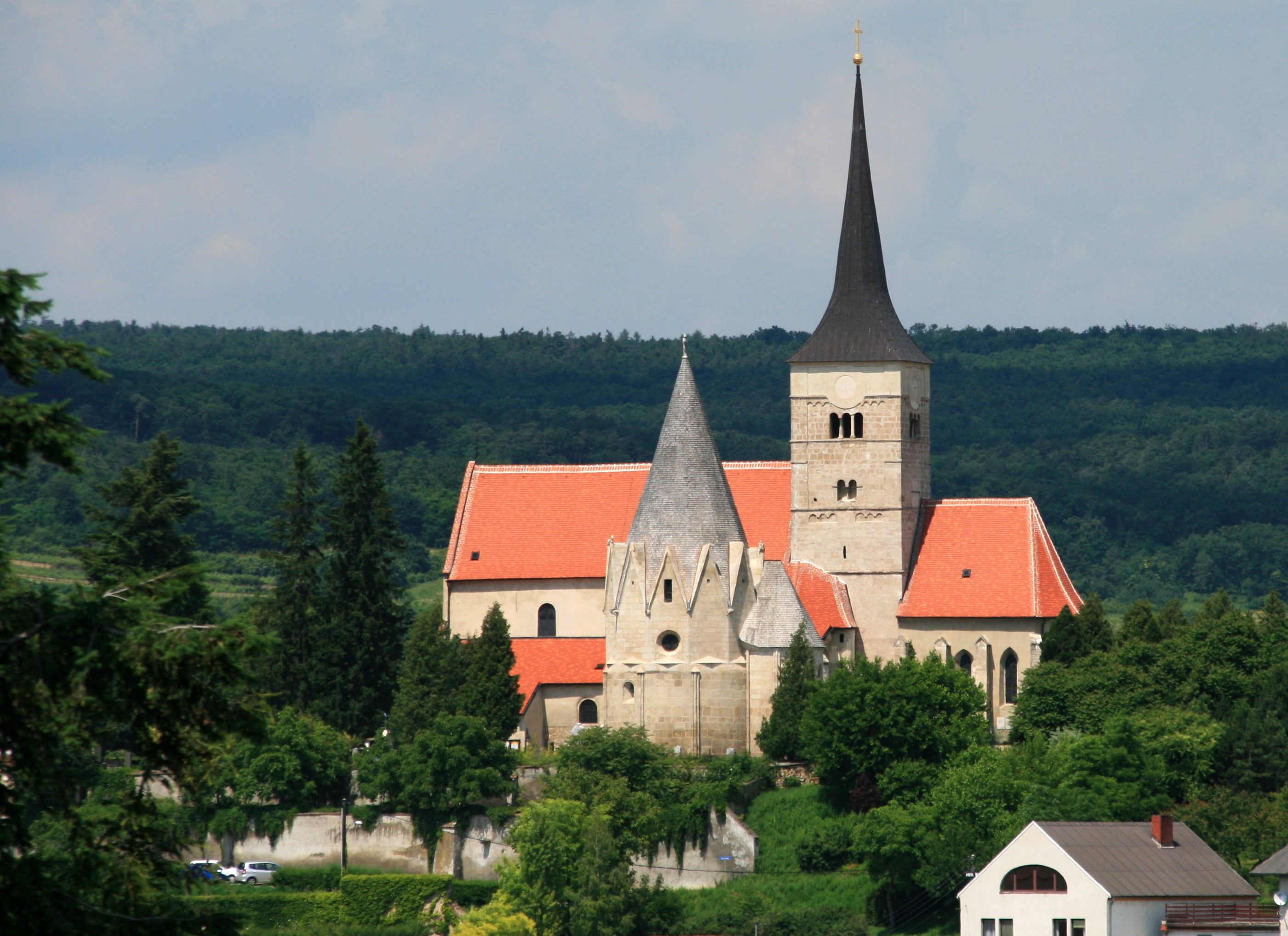 St. Michaelskirche in Pulkau mit rotem Dach und spitzem Turm, umgeben von Bäumen.