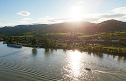 Die sanften Hügel der Wachau erstrahlen im warmen Licht der Abendsonne, während die Donau friedlich dahinfließt. Ein Boot gleitet über das glitzernde Wasser und lädt dazu ein, die atemberaubende Landschaft zu genießen, die von Weinbergen und charmanten Dörfern geprägt ist.