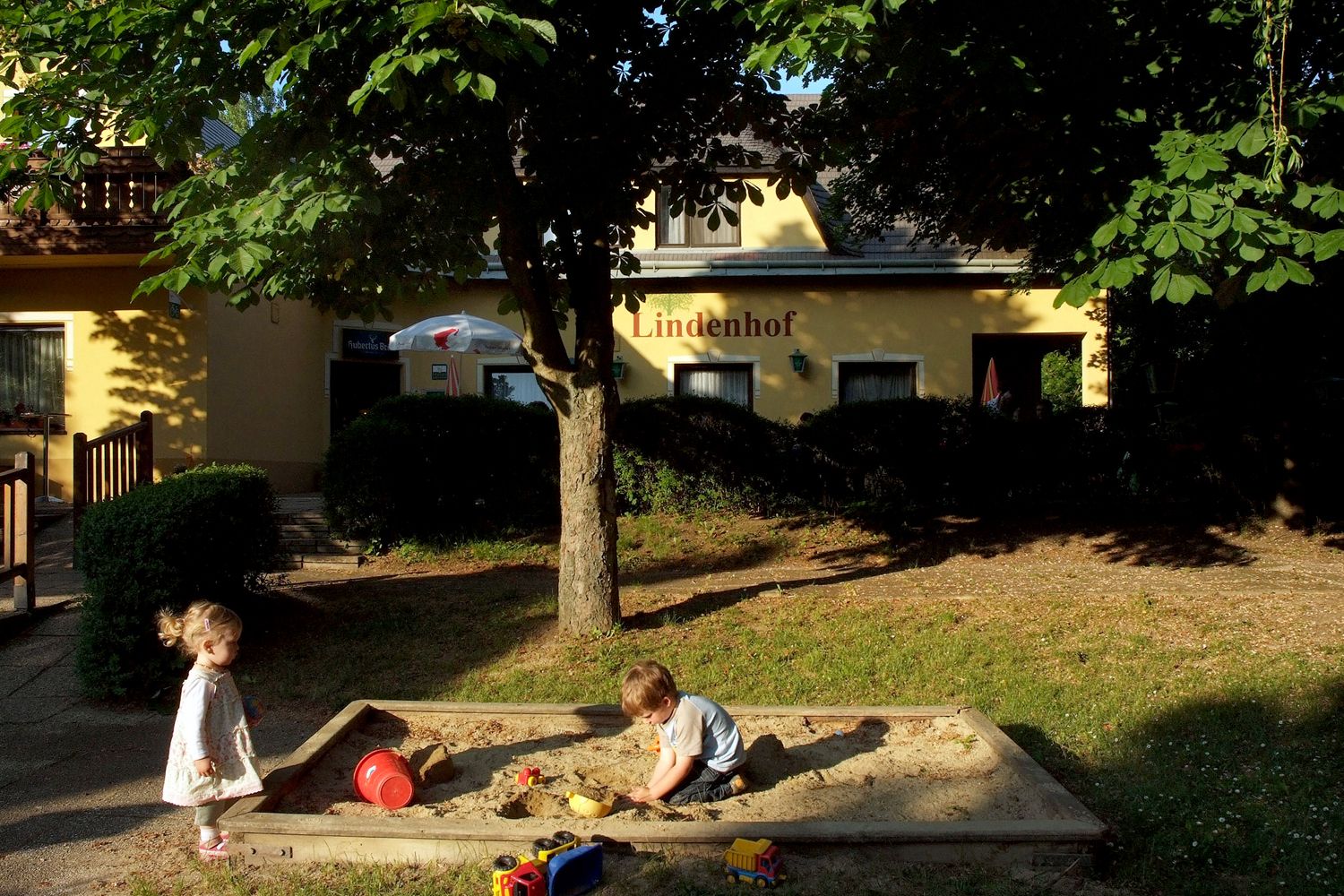 Zwei Kinder spielen im Sandkasten vor einem Gebäude mit der Aufschrift 'Lindenhof'.