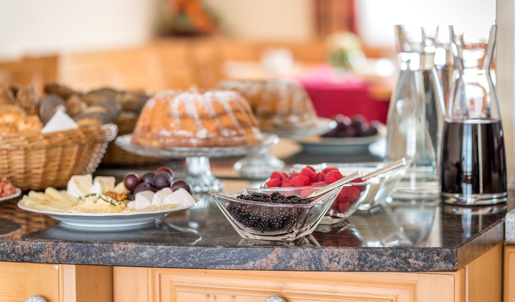 Frühstücksbuffet mit Kuchen, Beeren, Käseplatte und Getränken auf einem Tisch.