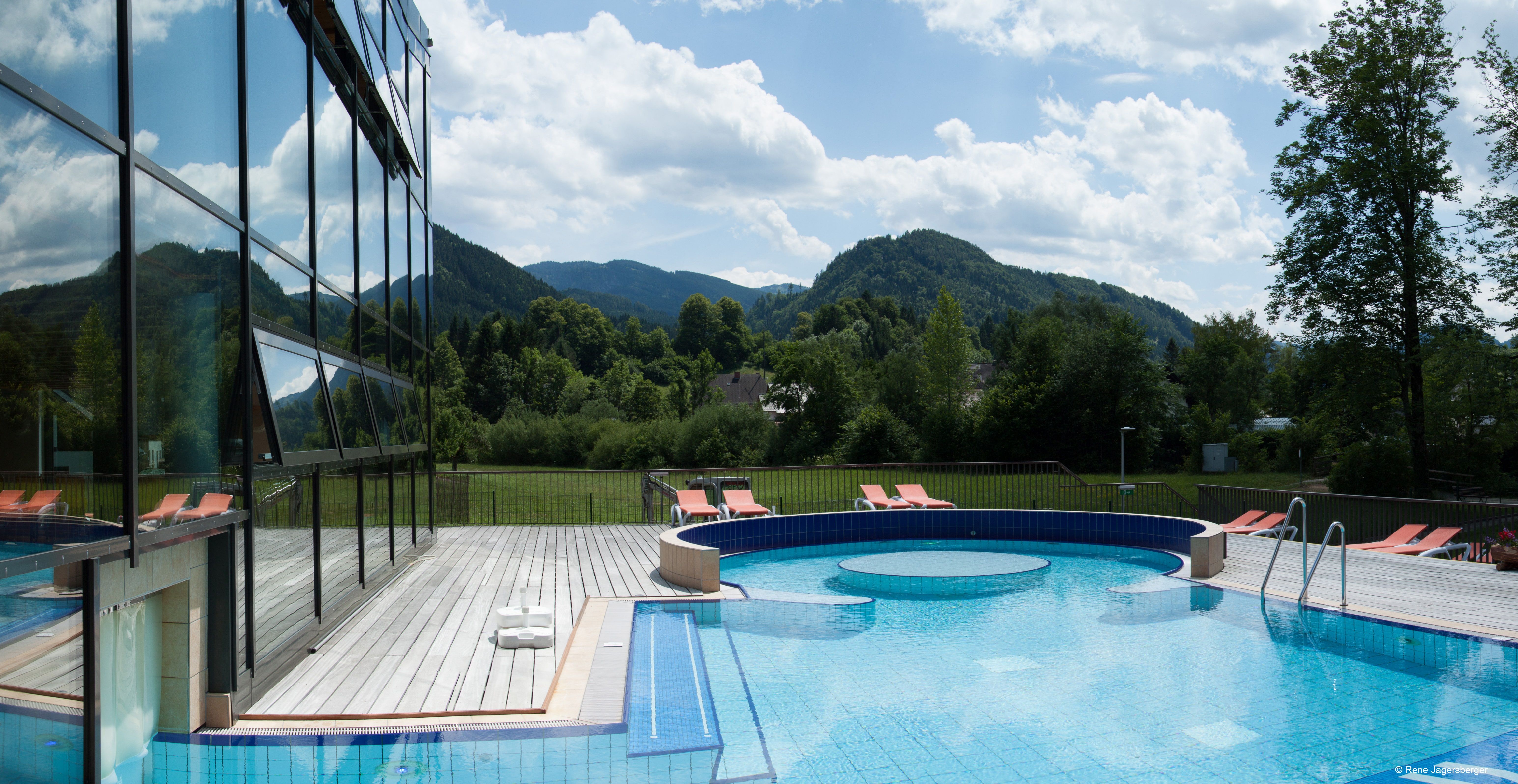 Außenbereich des Ybbstaler Solebads mit Pool und Liegestühlen, umgeben von grünen Hügeln und Bäumen.