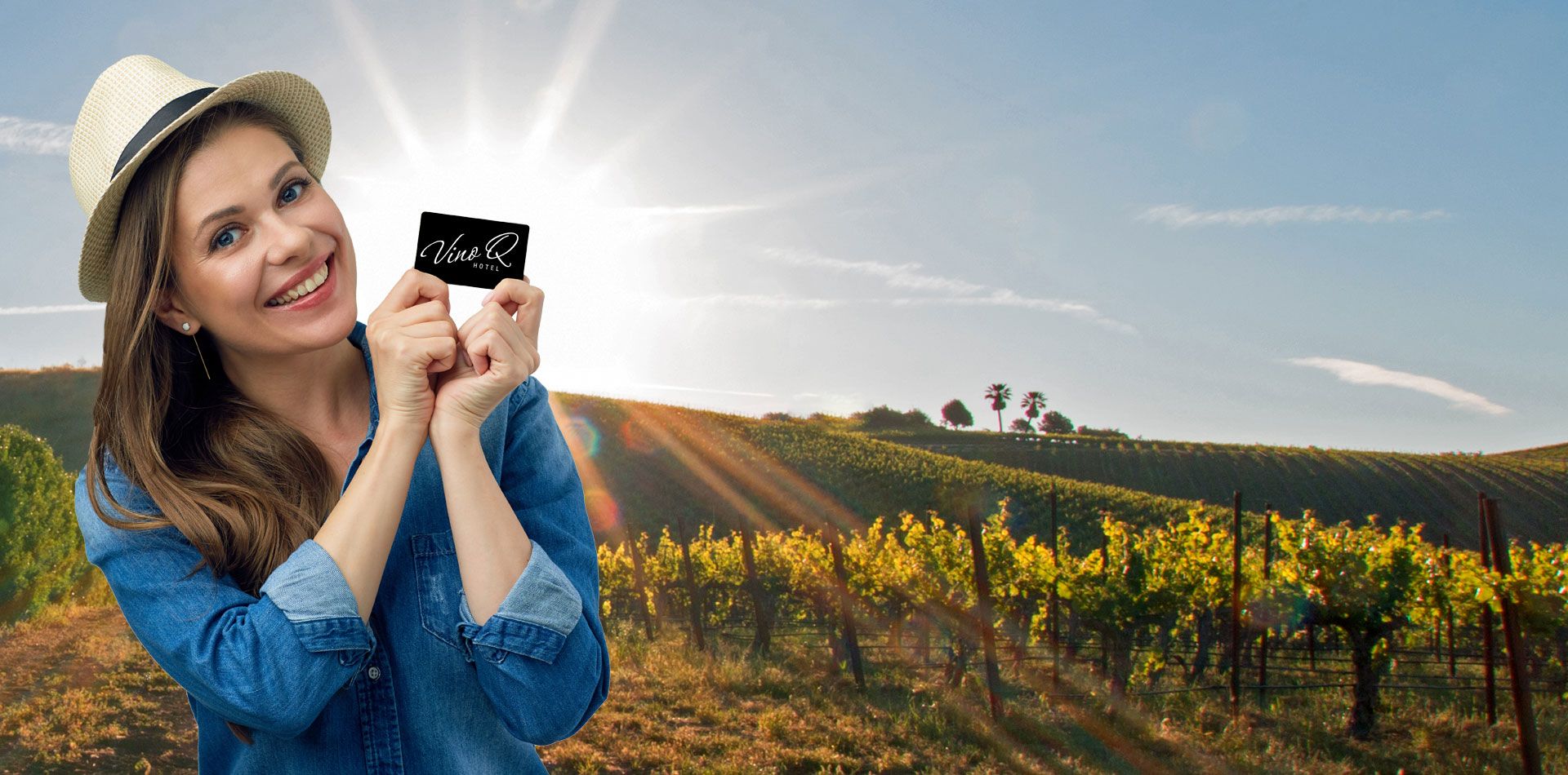 Frau mit Hut hält VinoQ-Karte vor einem sonnigen Weinberg.