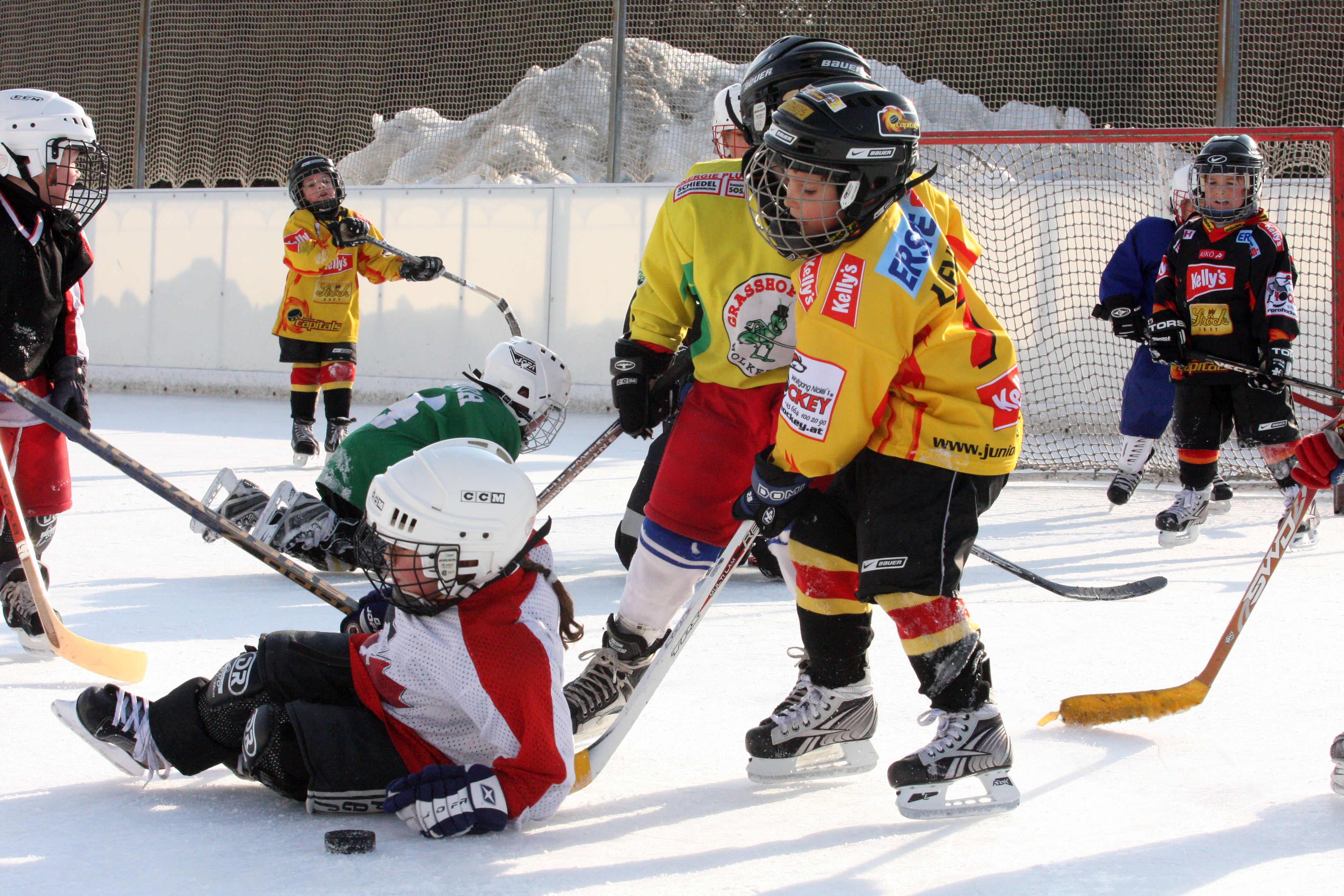 Kinder spielen Eishockey auf einer Außenbahn.