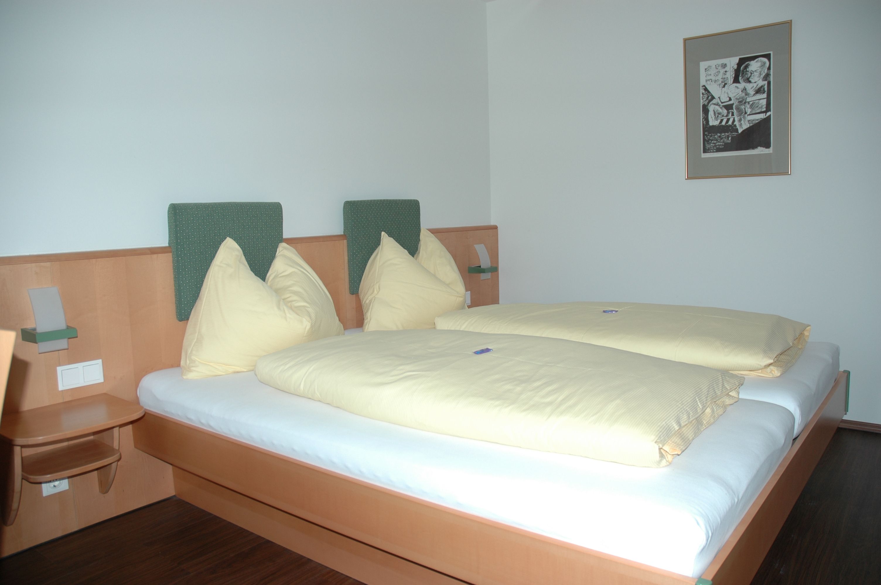 Hotelzimmer mit Doppelbett, gelber Bettwäsche und Wandbild.