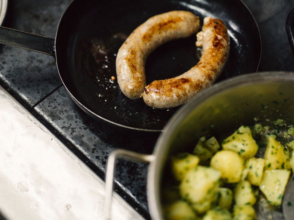 Bratwurst in Pfanne mit Kartoffeln im Topf.